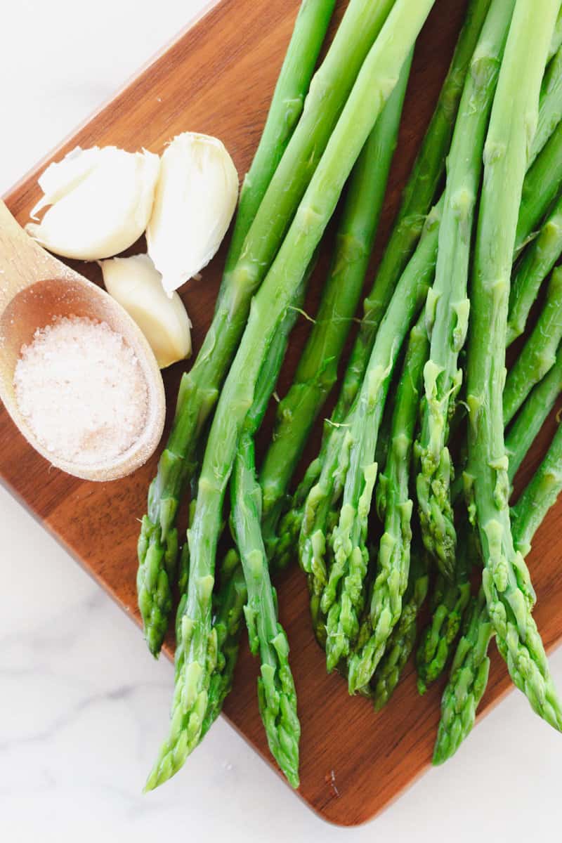 Boiled asparagus with a teaspoon of salt and garlic cloves next to it.