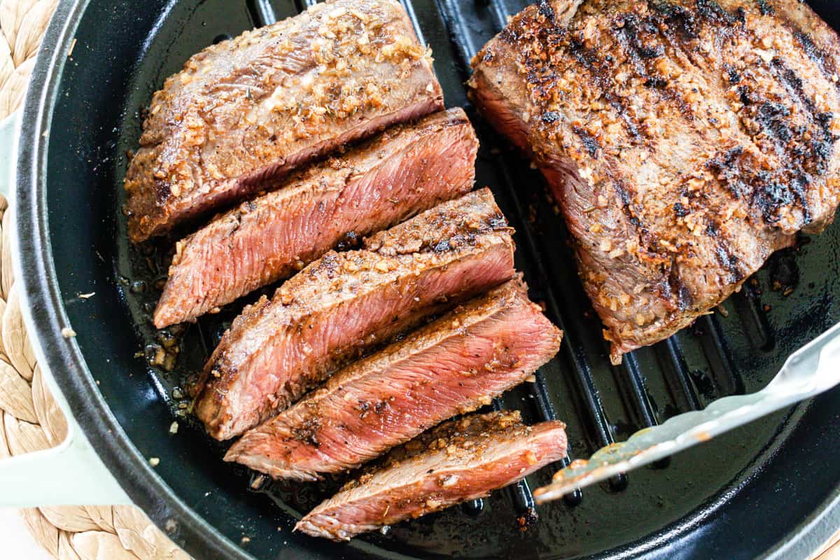 Flat iron steak sizzling on a  cast iron grill skillet.