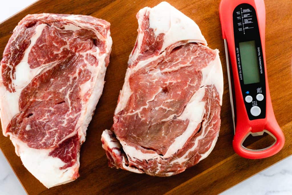 Two ribeye steaks on a wooden cutting board with an internal thermometer.