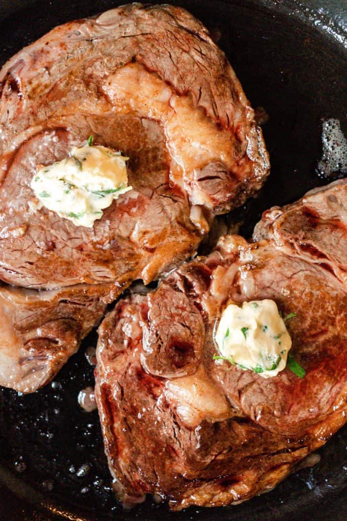 Two Ribeye steaks searing on a cast iron skillet.