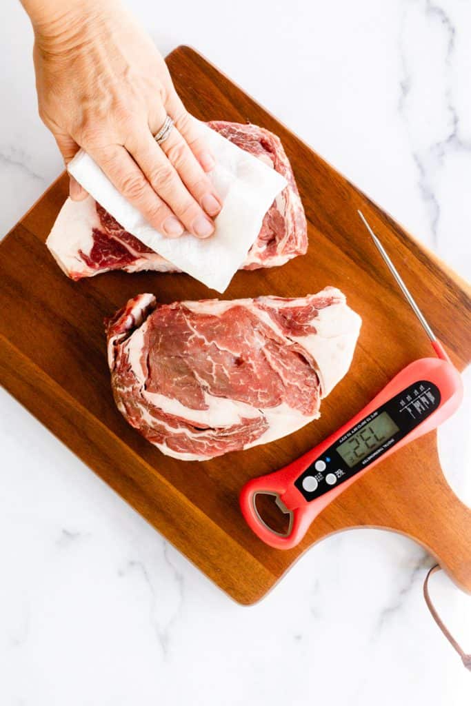 Patting down a ribeye steak with a paper towel to allow for a perfect sear.