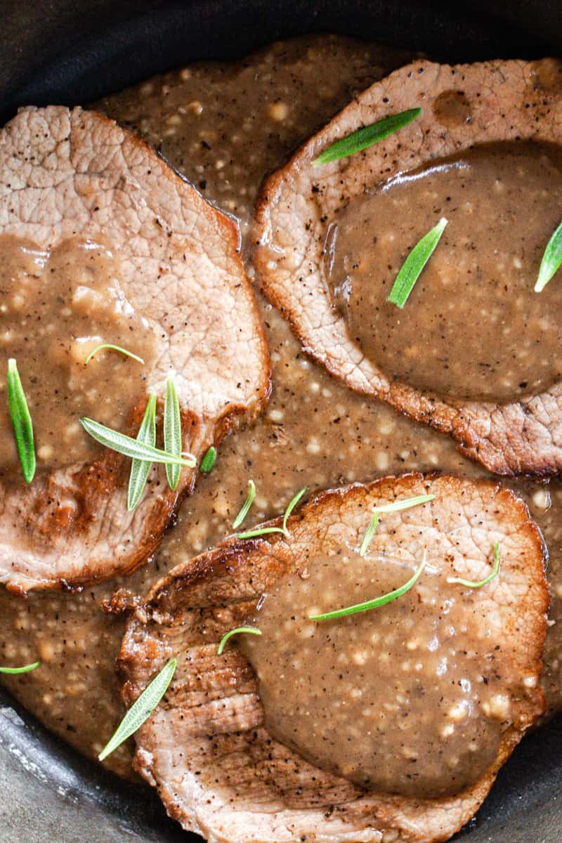 Juicy eye of round steak with fresh rosemary and gravy smeared on top.