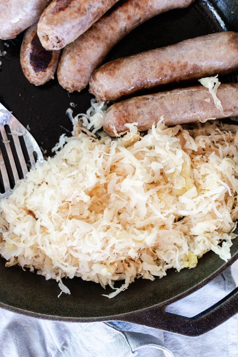 Cooking on a cast iron skillet are brats and sauerkraut. 