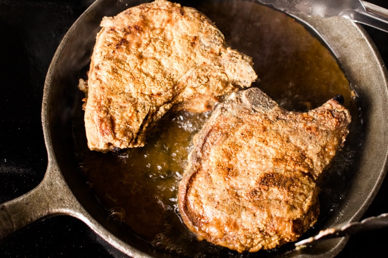 Pork chops sizzling in a cast iron skillet.