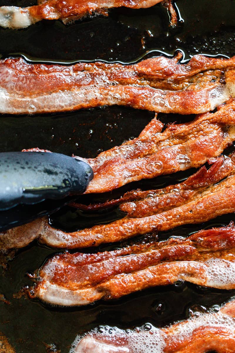 Flipping cast iron bacon with tongs.