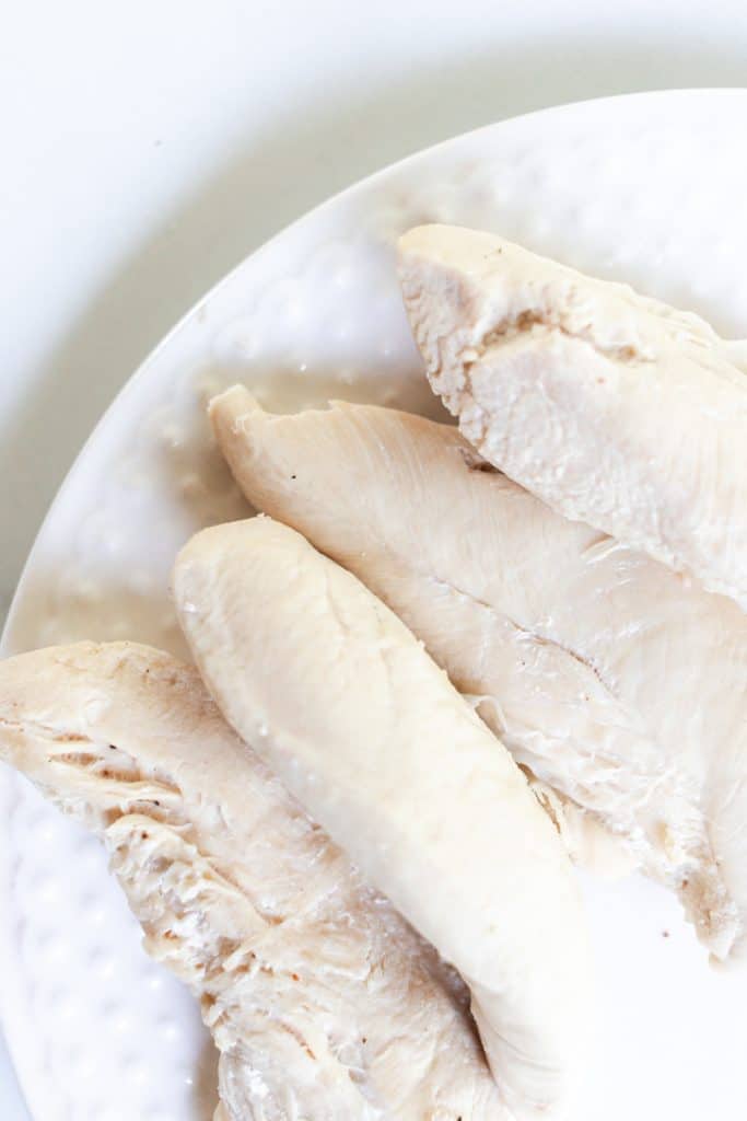 Boiled chicken tenders on a white plate cooling.