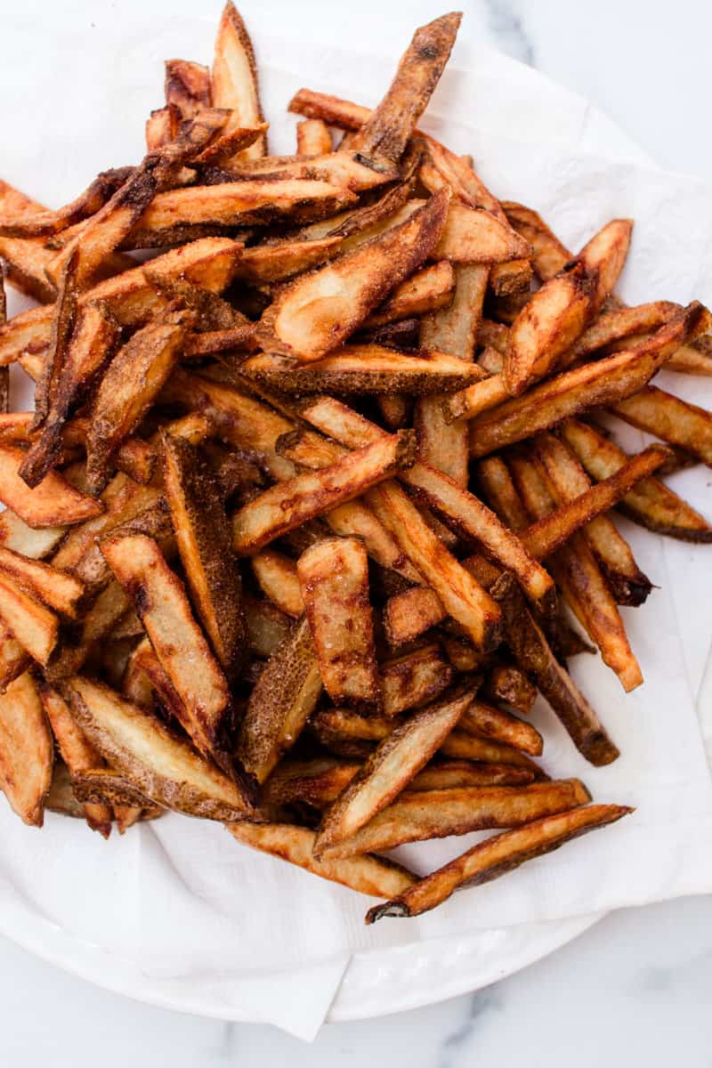 Fresh out of the fryer sitting on a napkin over a glass plate are the crispest homemade fries. 