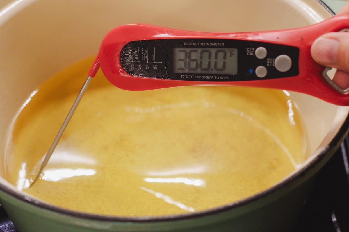 Red thermometer testing the temperature of heating peanut oil in a dutch oven.