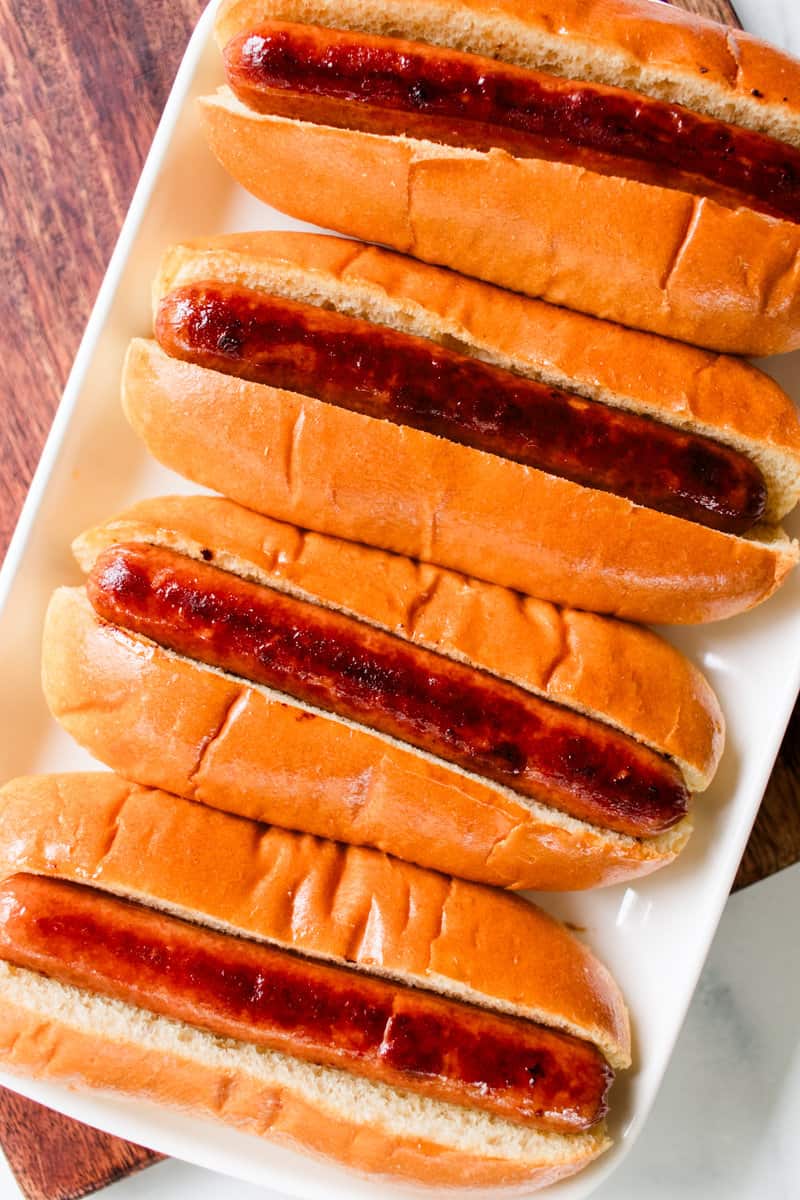 Hot dogs in buns lined on a white rectangle serving platter.