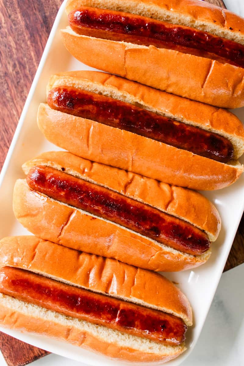 Hot dogs in buns lined on a white rectangle serving platter. 