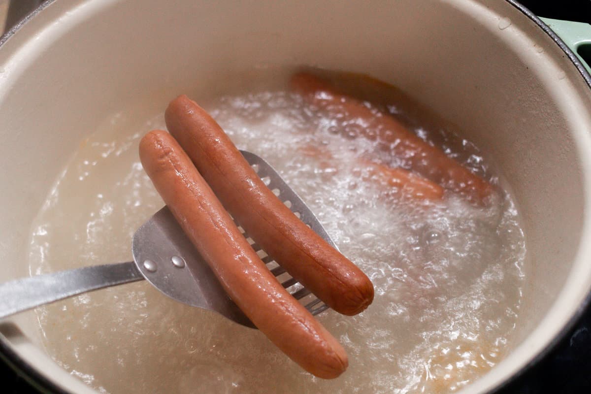 Boiling hot dogs in a cream colored dutch oven.