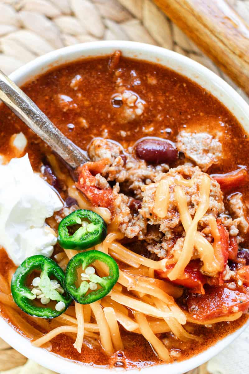 Delicious bowl of pork chili topped with shredded cheese, sour cream, and fresh jalapenos. 