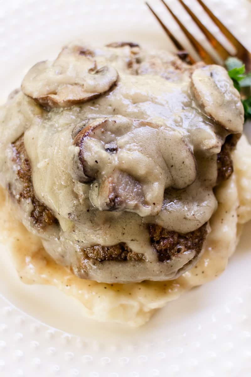 Smothered in gravy is a hamburger steak on a glass plate. 