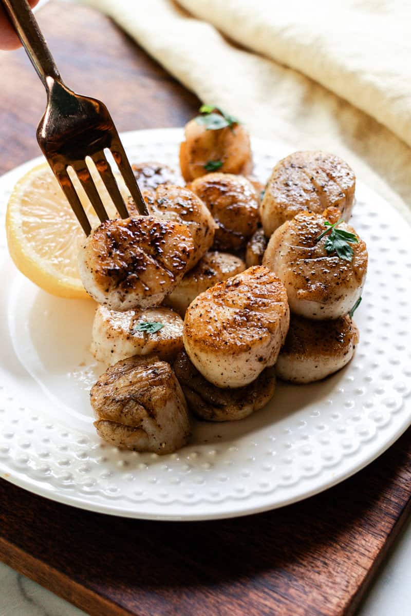 Fresh cooked scallops with salt and pepper on a white plate.