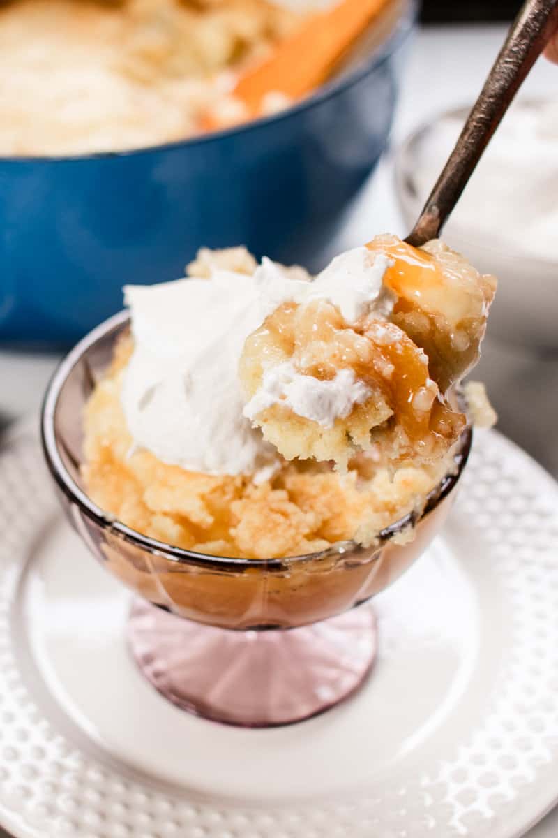 Peach dump cake in a dessert bowl topped with whip cream. 