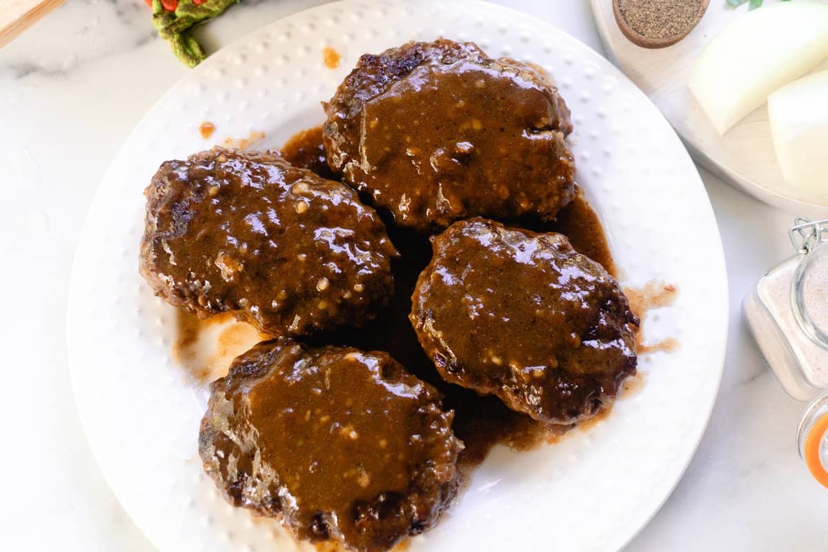 Salisbury steak on a white plate covered in french onion soup. 