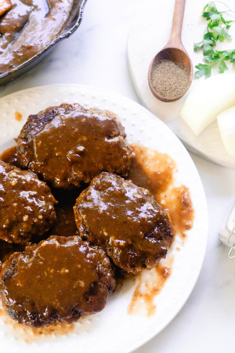 French onion soup and salisbury steak on a glass plate with seasoning on a wooden spoon in the corner. 