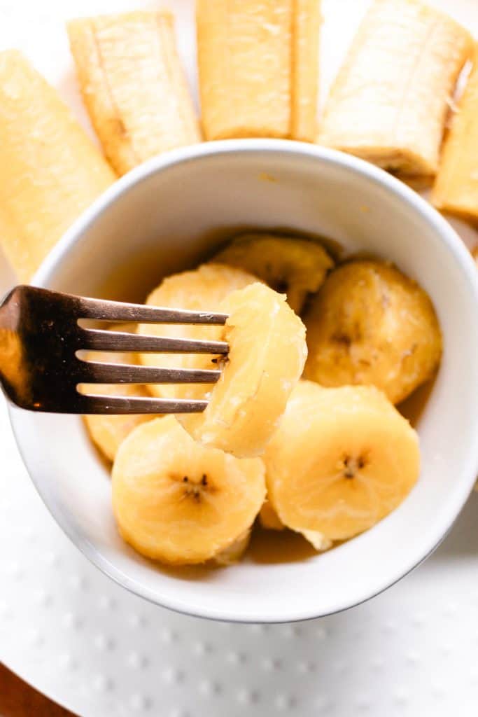 Shoving a fork into a sliced plantain to check check for tenderness after cooking.