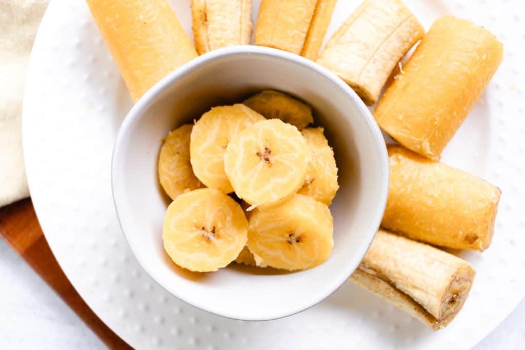 Boiled plantains sliced into thin pieces and placed into a white bowl.