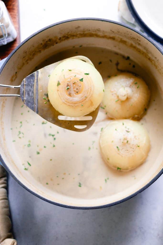 Scooping an onion out of the pot with a large spoon.