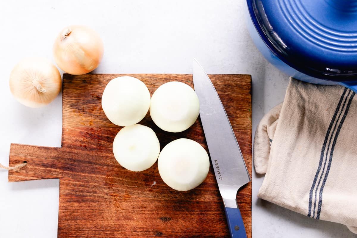 Trimming 4 onions on a wooden cutting board.