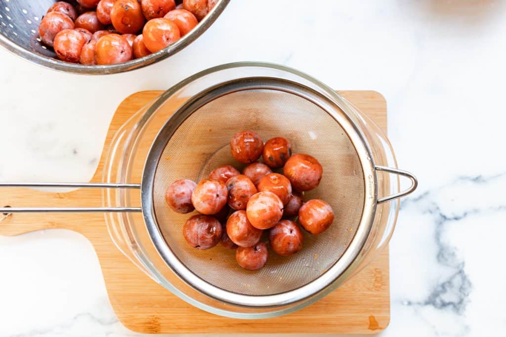 Placing persimmons in a metal strainer over a bowl. 