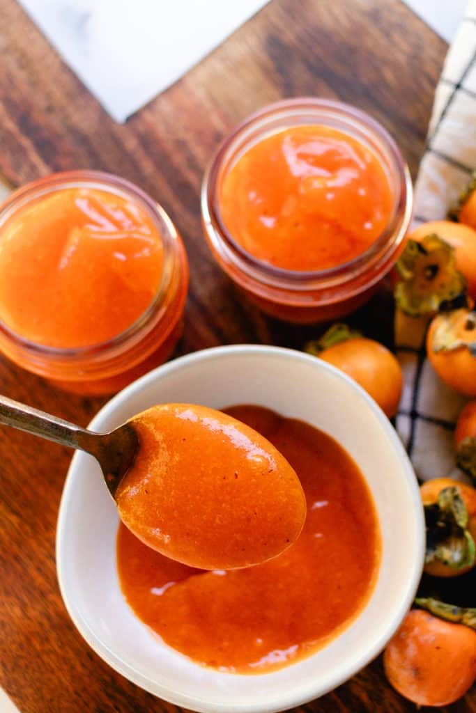 A spoonfull of persimmon puree made fresh with several jars of pulp in the background.