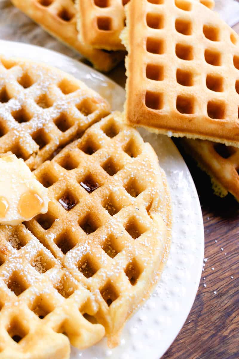 A stack of waffles made without milk in the background with a close up shot of the waffle and all its fixings.