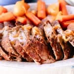 Thinly sliced moose roast on a white plate with carrots and potatoes.
