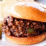 A venison sloppy joe sandwich on a white plate with a pickle.