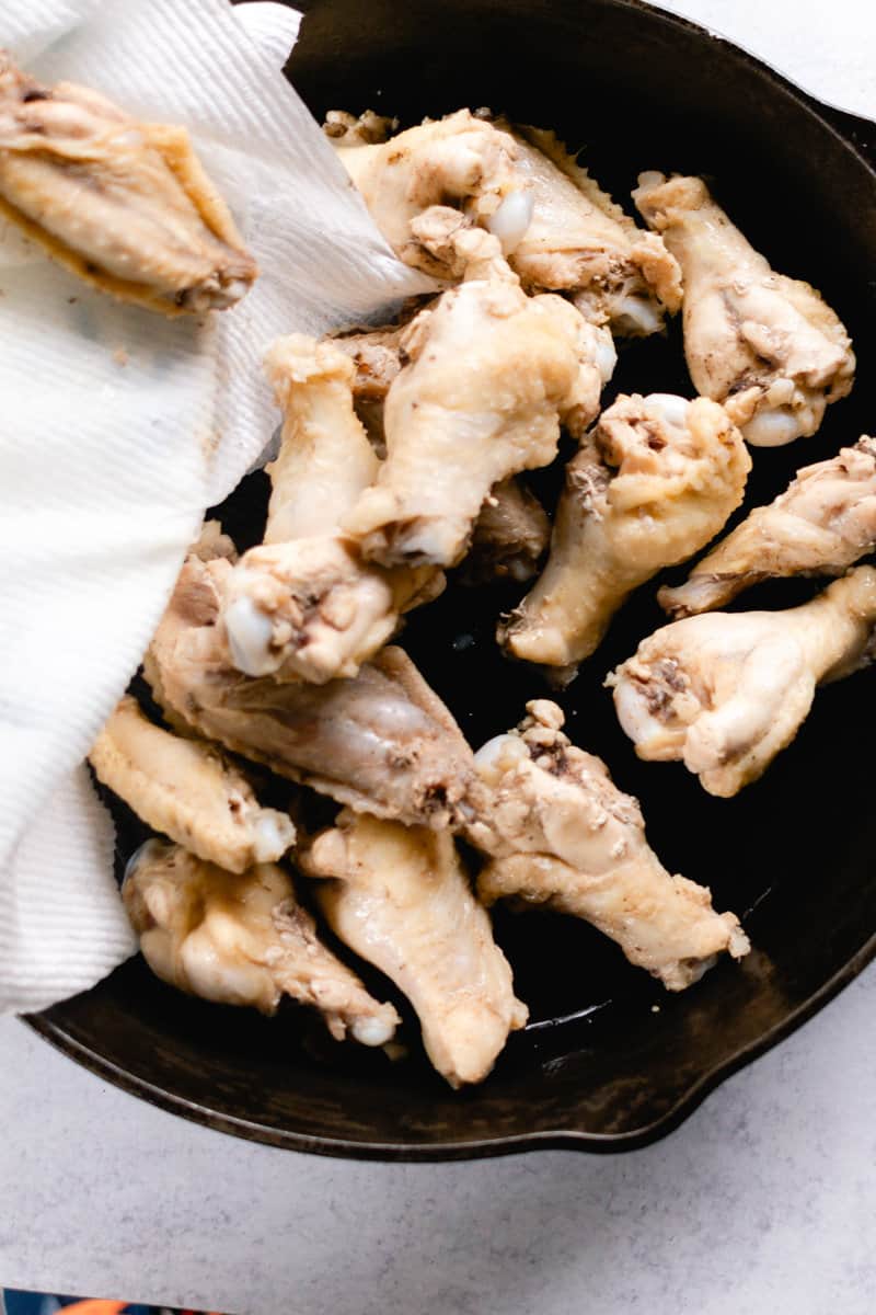 Transferring boiled wing to a cast iron skillet to get crispy in the oven.