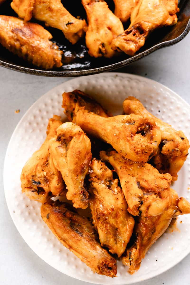 On a serving plate and in a skillet are cooked chicken wings. 