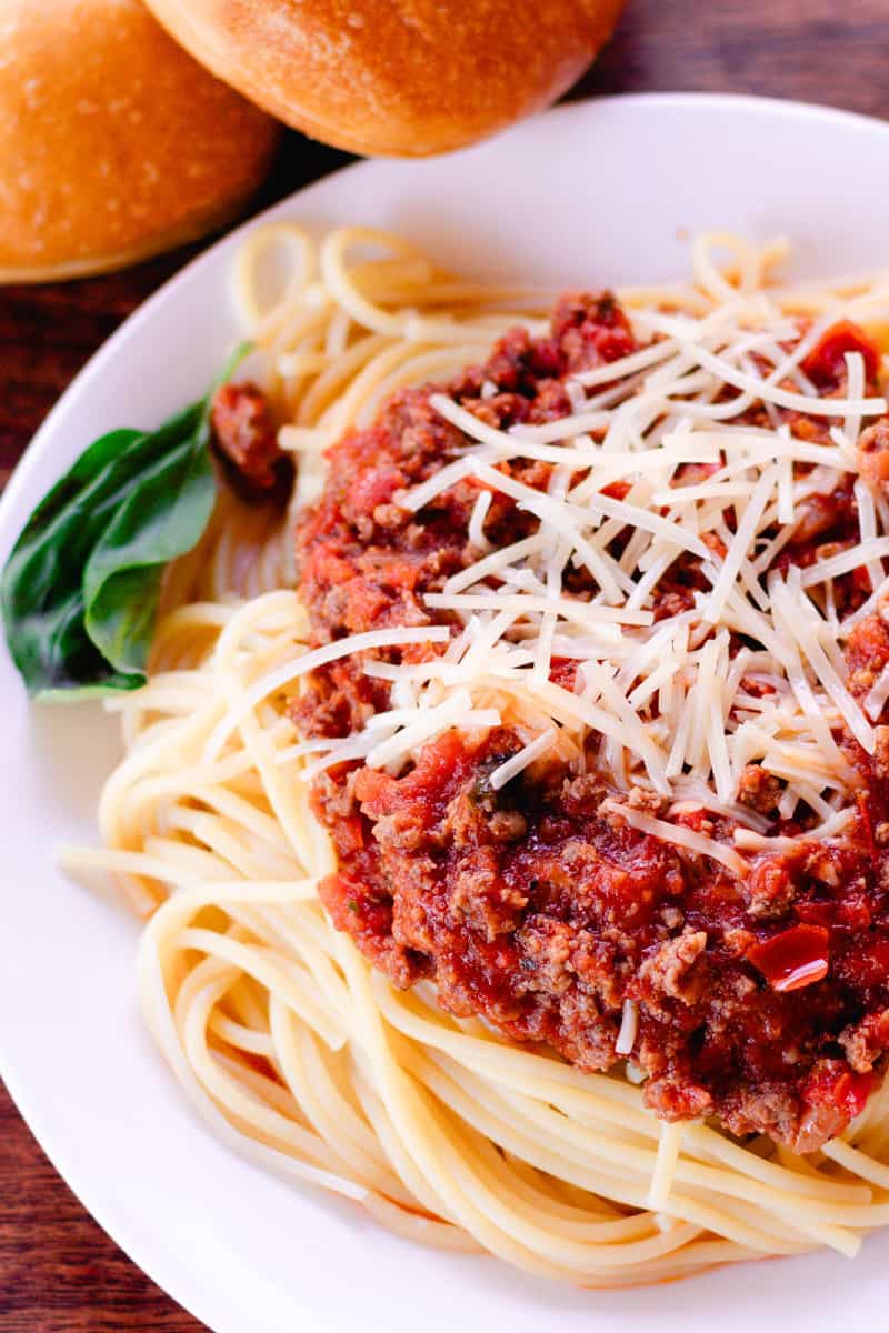 Venison pasta with parmesan cheese and two rolls on the side.