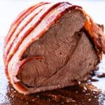 An elk roast cut in half after it has cook and it is wrapped in bacon.