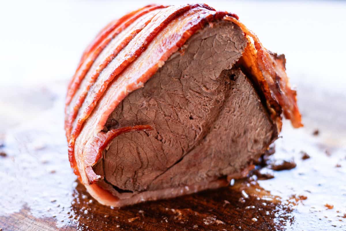 An elk roast cut in half after it has cook and it is wrapped in bacon.