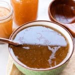 Broth in a serving bowl on the counter with a wooden spatula and jars of broth on the side.