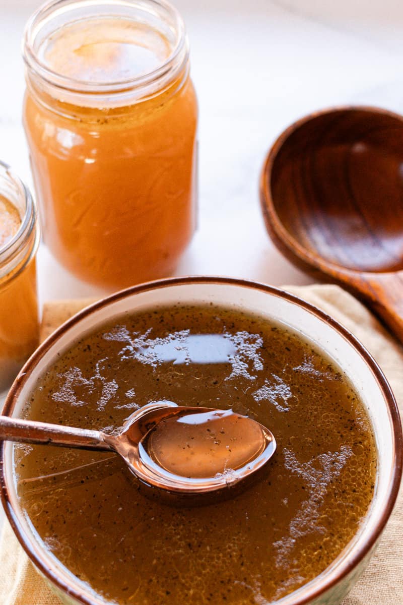 Oxtail bone broth in a glass bowl with a brown rim and a spoon in the bowl.