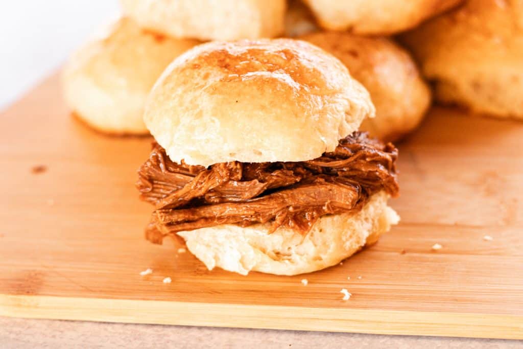 Juicy pulled venison sandwich on a homemade roll with more rolls in the background.