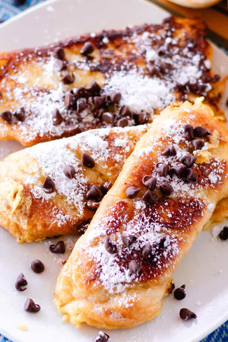 3 slices of brioche french toast on a white plate with powdered sugar and chocolate chips on top. 