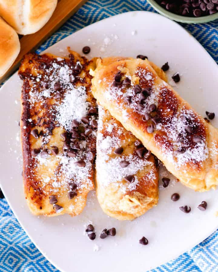 3 slices of chocolate chip brioche french toast on a white plate sprinkled with powdered sugar.