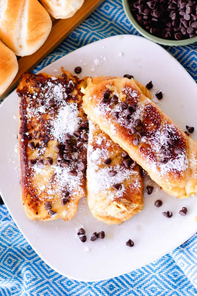 3 slices of chocolate chip brioche french toast on a white plate sprinkled with powdered sugar.