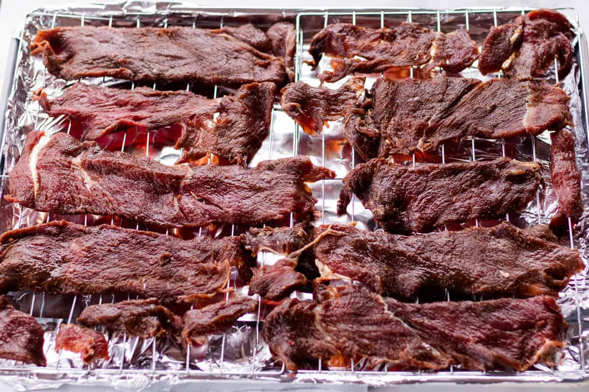 Lining the elk jerky on a wire rack over an aluminum foil lined baking sheet.