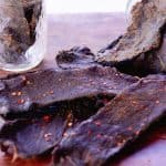 Tender elk jerky on a wooden table with several pieces in the background.