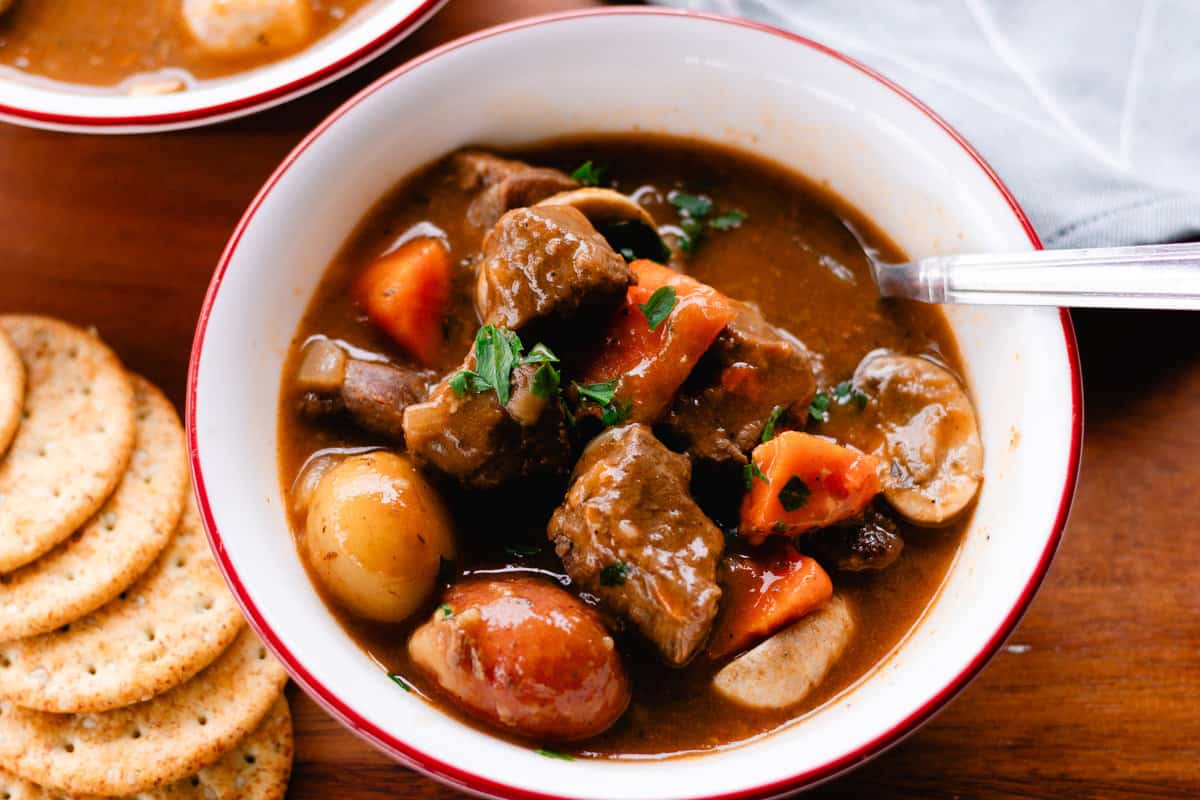 Hearty elk stew with thick chunks of elk meat, carrots and potatoes on a wooden table.