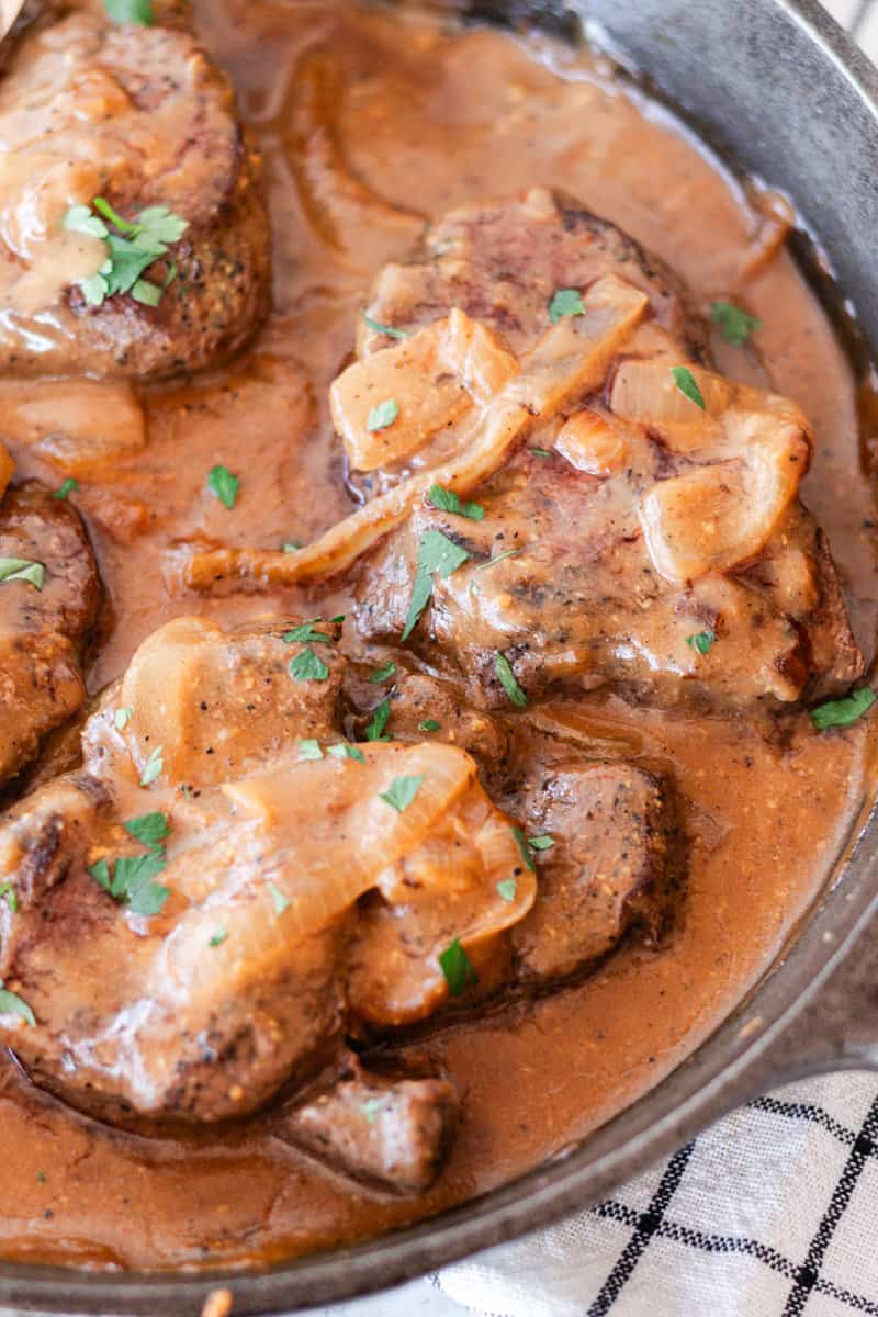 Smothered moose chops in a thick dark gravy in a cast iron skillet with green garnishings.
