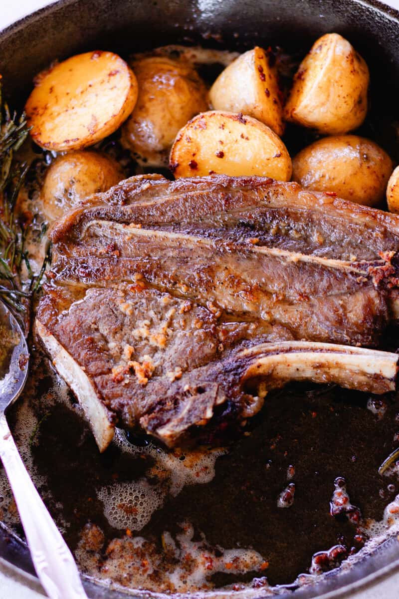 Cast iron cooked lamb chop with roasted potatoes and fresh rosemary on the side.