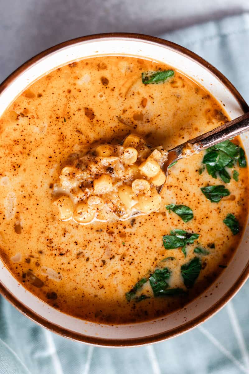 Creamy soup de maiz in a small bowl with a brown rim and a bronze spoon.