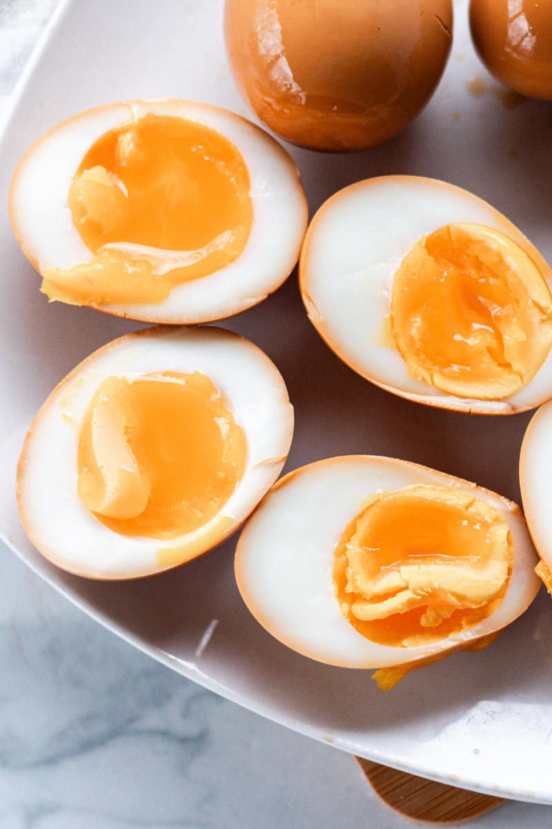Soy sauce eggs after they have marinated are on a serving dish with a few eggs in the background.