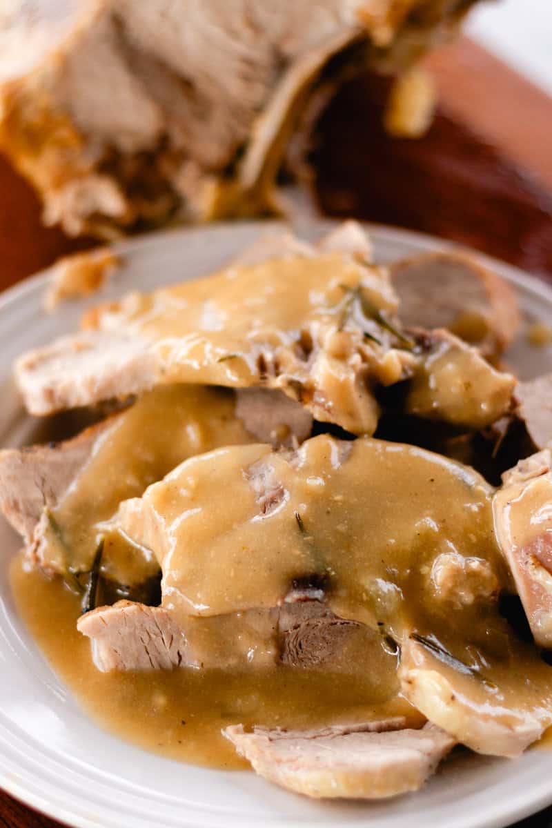 Braised pork loin roast sliced thinly on a plate with gravy.