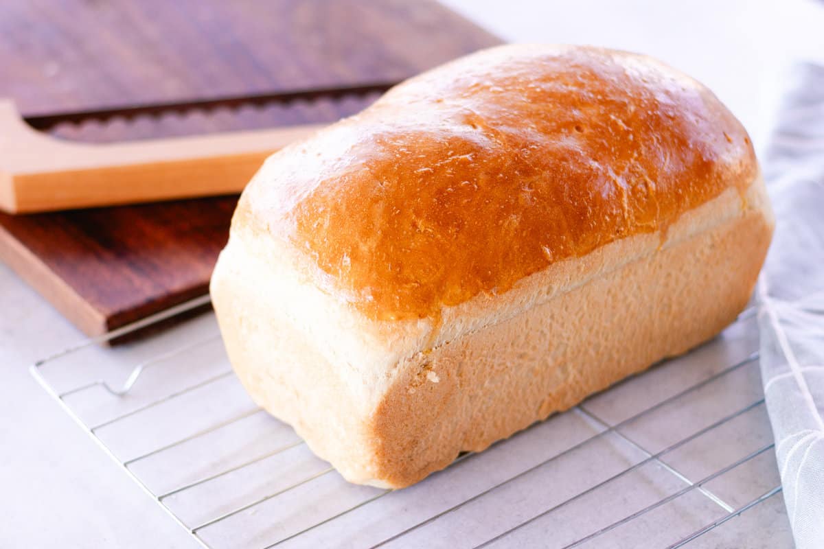 Cast iron loaf bread resting on a cooling rack with a cutting board in the back.